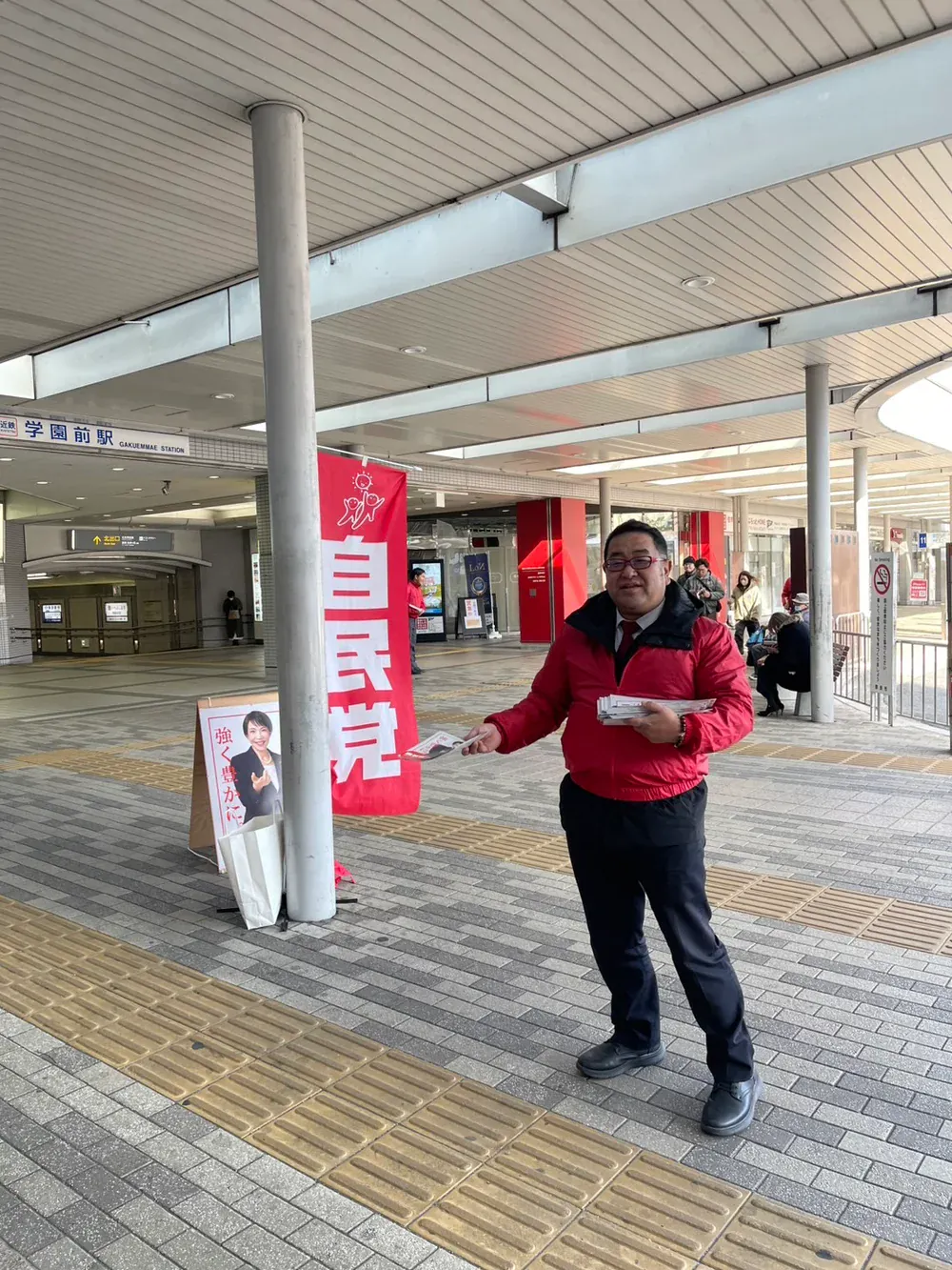 駅前で配布物を手にする鈴木たけし