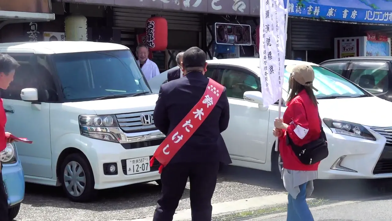商店の前で地域の方に向き合う鈴木たけし