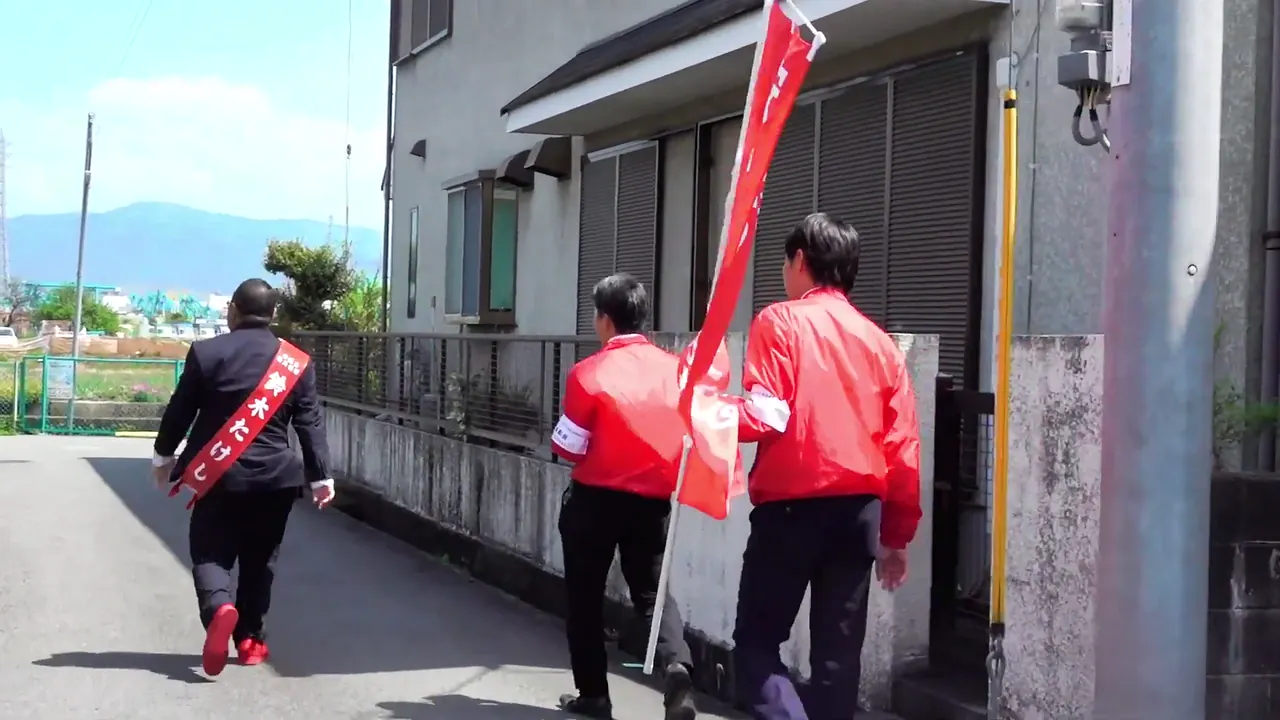 スタッフとまちを歩きながら手を振る鈴木たけし