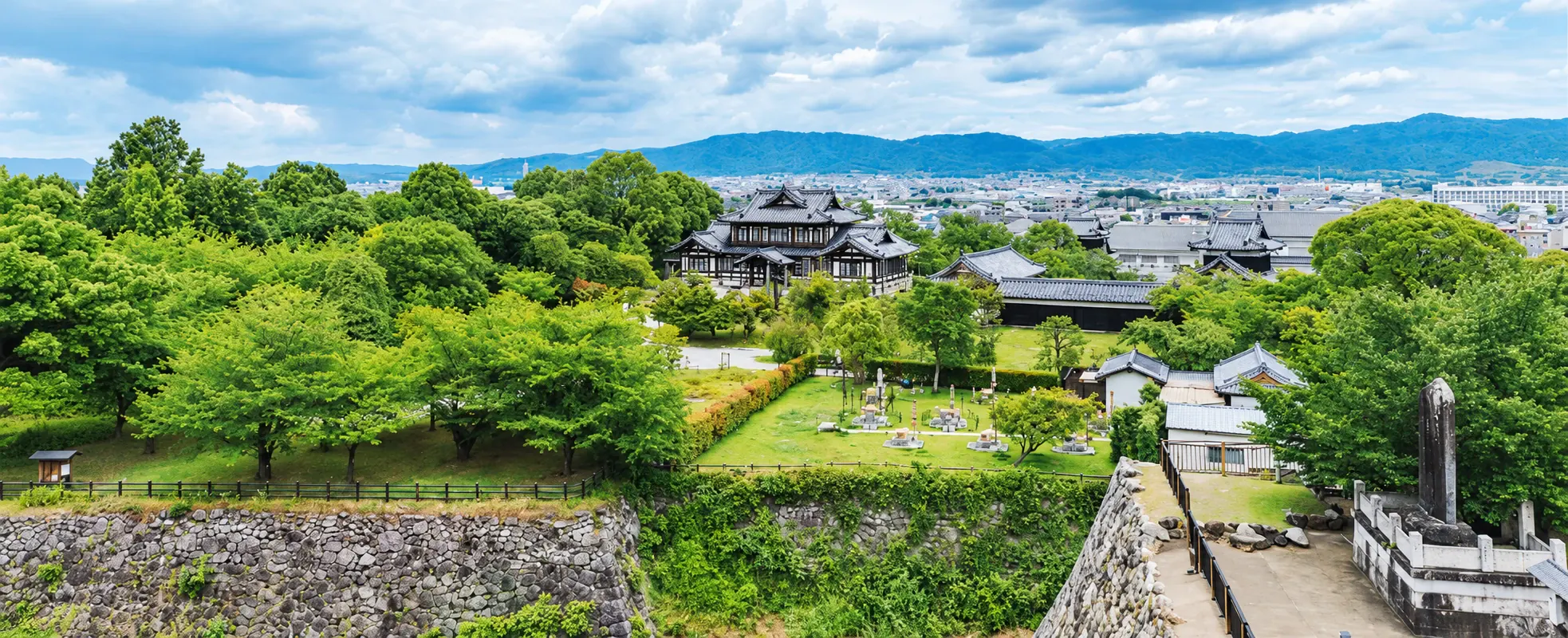 緑豊かな庭と石垣の向こうに、まちと山並みを望む風景